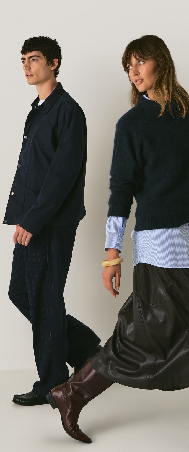 Veste en coton bleu marine, pantalon à rayures bleu marine sur un modèle masculin. Modèle féminin portant un pull en tricot sombre, une chemise rayée bleue, une jupe en cuir marron et des bottes.