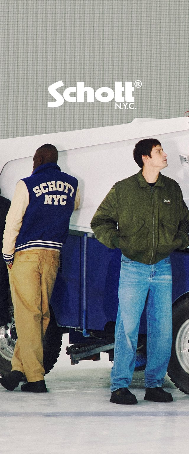 Zwei Personen stehen neben einem blauen Fahrzeug. Eine trägt eine marineblaue Varsity-Jacke mit "Schott NYC" und beigen Hosen; die andere hat eine grüne Bomberjacke und blaue Jeans an.