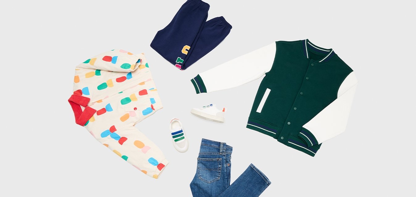 Pestrobarevná bunda s kapucí a červenými akcenty, námořnické tepláky, modré džíny, bílé boty a zeleno-bílá varsity bunda na světlém pozadí.