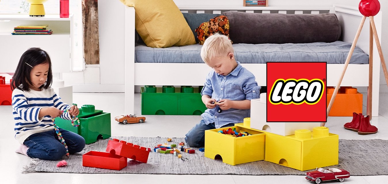 Dvě děti sedí na podlaze a hrají si s velkými barevnými stavebnicemi v jasné, moderní herně.