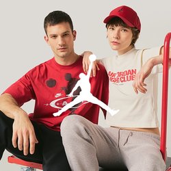 Dva mladí dospělí sedí na červeném plošinovém vozíku; jeden má na sobě červené tričko s grafikou, druhý bílé krátké tričko a červenou čepici.