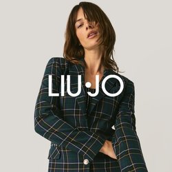 Žena pózující v kostkovaném saku a černých kalhotách s flitry na jednobarevném světlém pozadí.