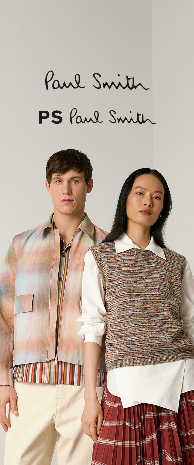 Zwei Models stehen vor einem neutralen Hintergrund mit „Paul Smith“-Logos darüber; der Mann trägt eine pastellfarbene Jacke, die Frau trägt eine Strickweste und einen karierte Rock.