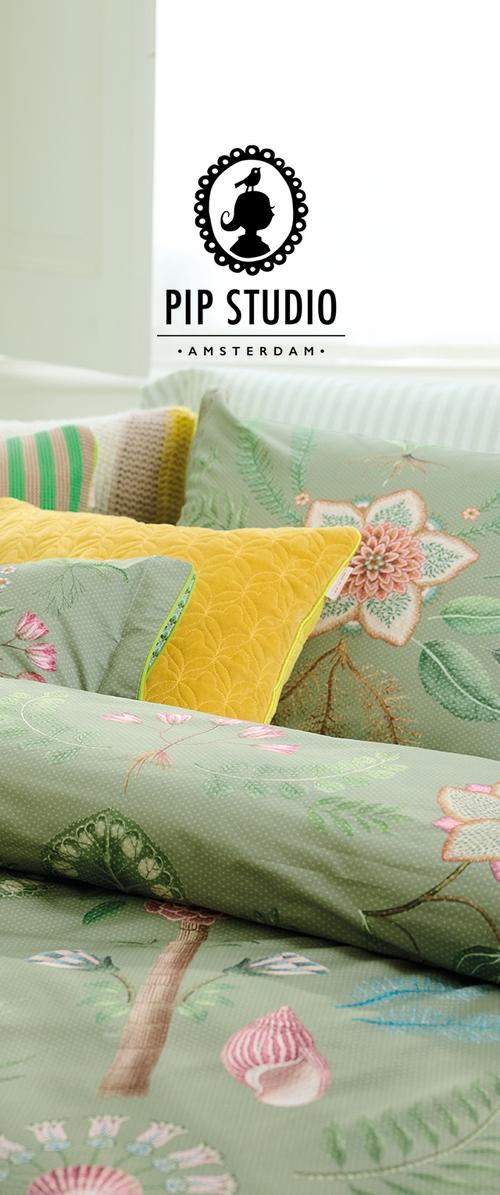 Parure de lit à motif floral vert avec des fleurs roses et jaunes brodées, accompagnée d'un coussin en relief jaune et d'un coussin en tricot rayé.