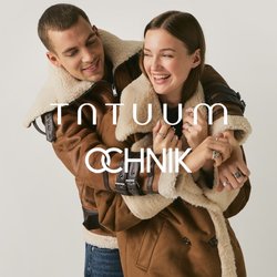 Mladý pár se usmívá a objímá, oba mají na sobě stejné hnědé kožené bundy s kožešinou na světlém jednobarevném pozadí.