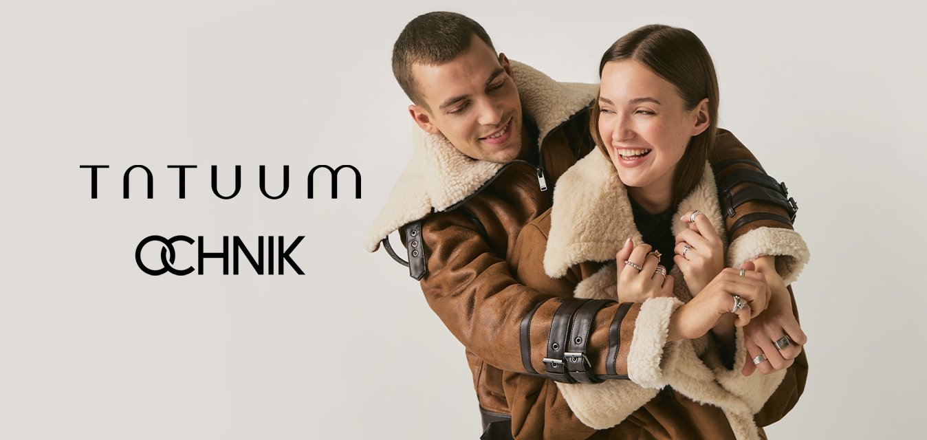 Mladý pár se usmívá a objímá, oba mají na sobě stejné hnědé kožené bundy s kožešinou na světlém jednobarevném pozadí.