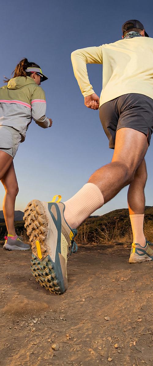 Zwei Personen laufen auf einem Naturpfad, tragen Sportbekleidung und Trailrunning-Schuhe unter klarem Himmel beim Sonnenuntergang.