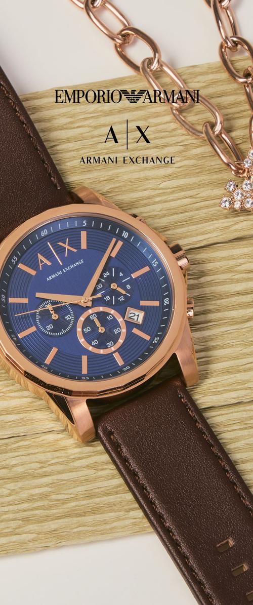 Montre-bracelet Armani Exchange en cuir marron avec cadran bleu et doré, posée sur une surface en bois, à côté d’un bracelet chaîne doré orné de cristaux.