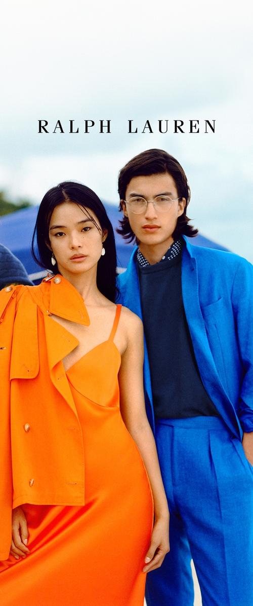 Vestido de satén naranja con detalles descubiertos en los hombros; chaqueta de traje azul con pantalones a juego. Ambas figuras en un entorno de playa.
