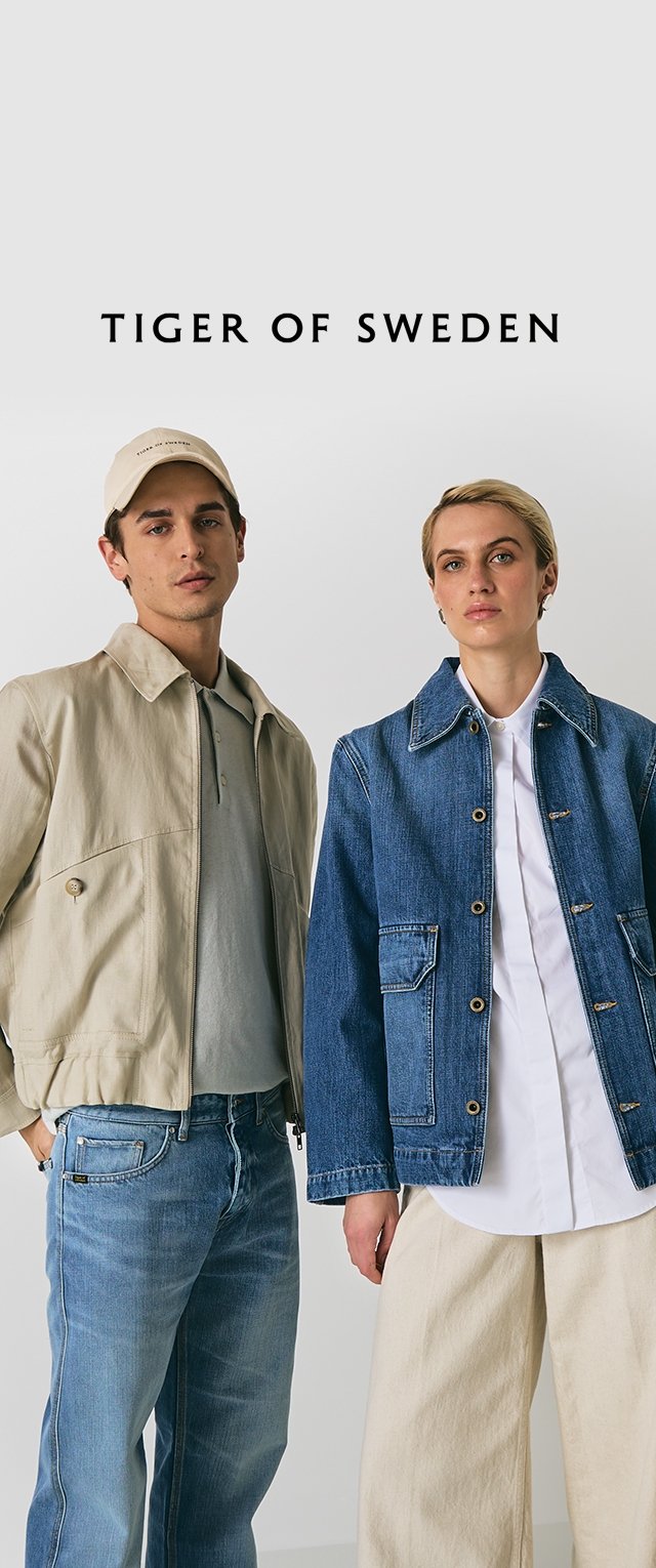 Hombre y mujer están de pie uno al lado del otro, vistiendo chaquetas informales; el hombre lleva una gorra y chaqueta beige, y la mujer lleva una chaqueta de mezclilla azul y una camisa blanca.