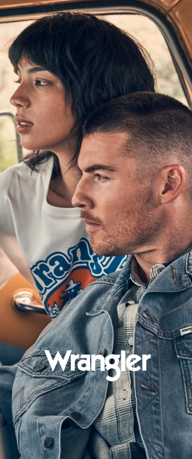 Joven hombre y mujer sentados juntos en un vehículo, ambos mirando hacia adelante; el hombre lleva una chaqueta vaquera y la mujer una camiseta blanca con gráfico.