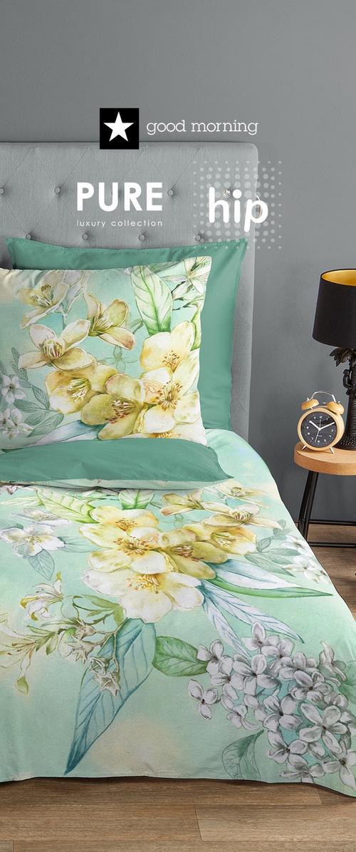 Bettwäsche-Set mit Blumenmuster, das aus leicht grünem Stoff mit gelben und weißen Blumen besteht, ergänzt durch passende einfarbige Kissen.