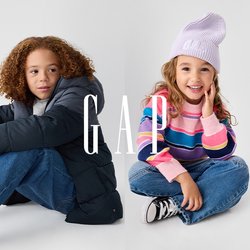 Dvě děti sedí na neutrálním pozadí. Jedno má na sobě tmavou prošívanou bundu a světle modré džíny; druhé má pruhovaný svetr a lila čepici.