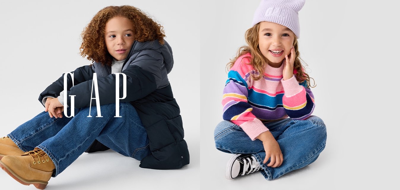 Dvě děti sedí na neutrálním pozadí. Jedno má na sobě tmavou prošívanou bundu a světle modré džíny; druhé má pruhovaný svetr a lila čepici.