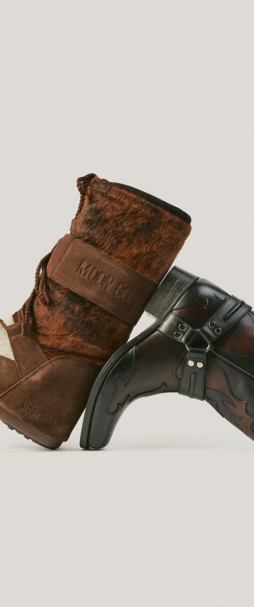 Moon Boot marron doublé de fourrure et botte western en cuir noir positionnés semelle contre semelle sur un fond neutre.