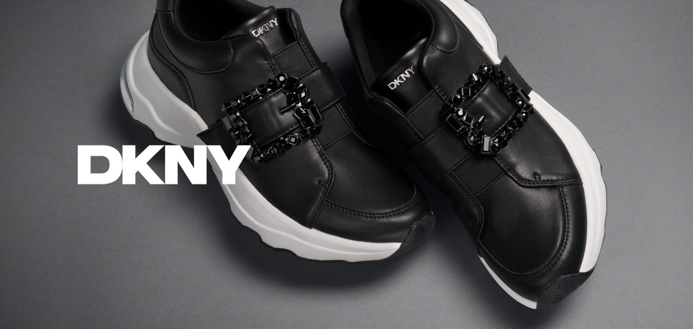 Černé slip-on tenisky s bílými masivními podešvemi a zdobnými černými krystalovými sponami na šedém pozadí.