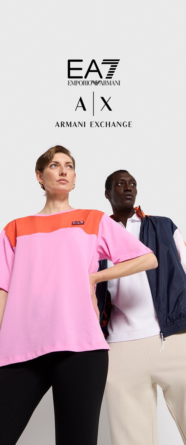 Camiseta rosa de gran tamaño con acentos naranjas en los hombros y logotipo. Leggings negros. Modelo con pelo corto y pendientes; modelo negro con una camisa blanca y un chaleco azul marino.