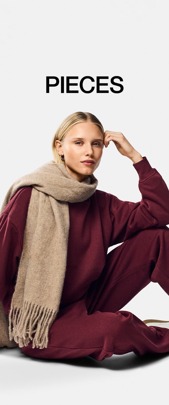 Écharpe beige tricotée avec des franges posée sur un sweatshirt bordeaux et un pantalon. Le modèle est assis de manière décontractée, mettant en valeur un design à coupe relaxée.
