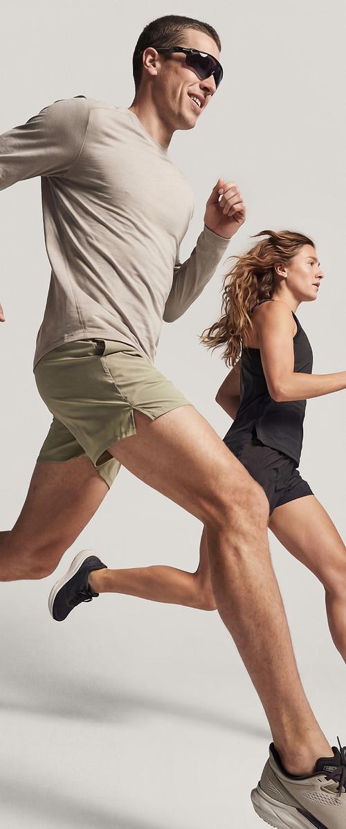 Un homme en lunettes de soleil et tenue de sport légère court aux côtés d'une femme vêtue de tenue de sport noire sur un fond uni.