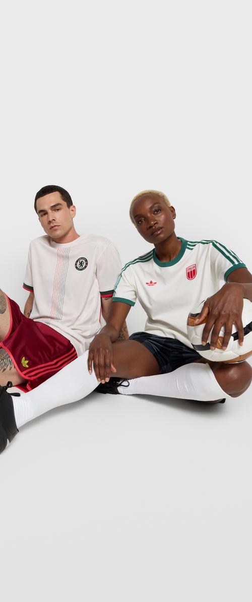 Deux personnes sont assises par terre, portant des maillots de sport. Le premier maillot est blanc avec des détails noirs, le second est blanc avec des accents rouges.