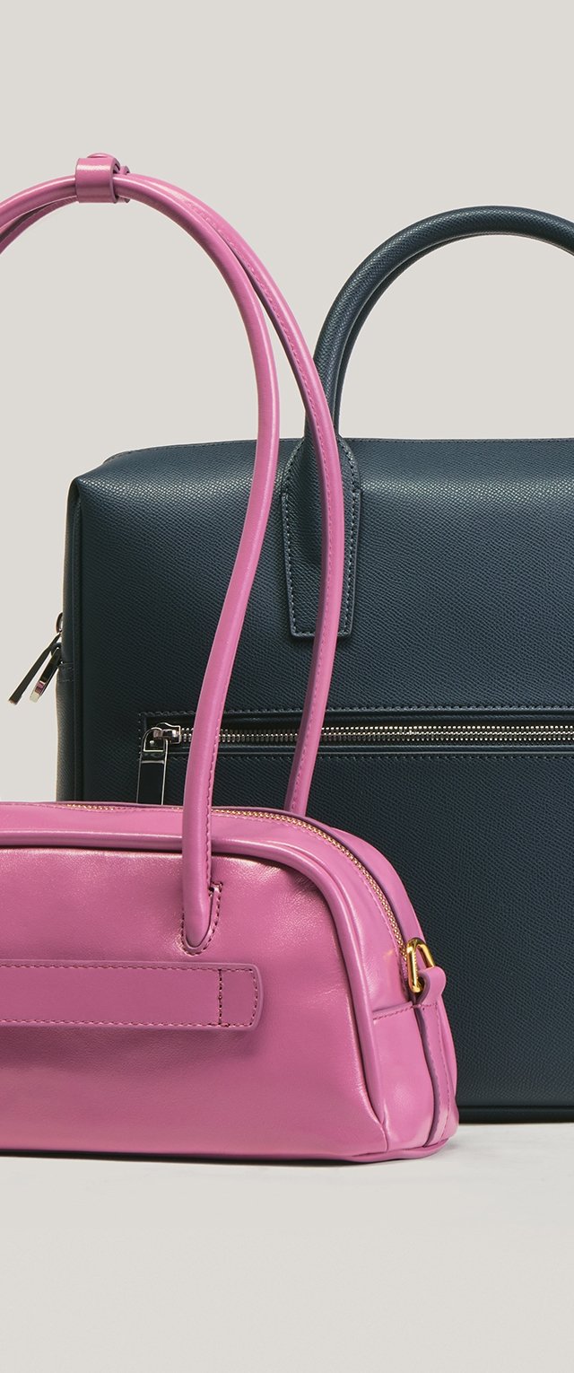 Bolso de cuero rosa con asas largas delante de un bolso de cuero negro texturizado con asa corta y bolsillo con cremallera.