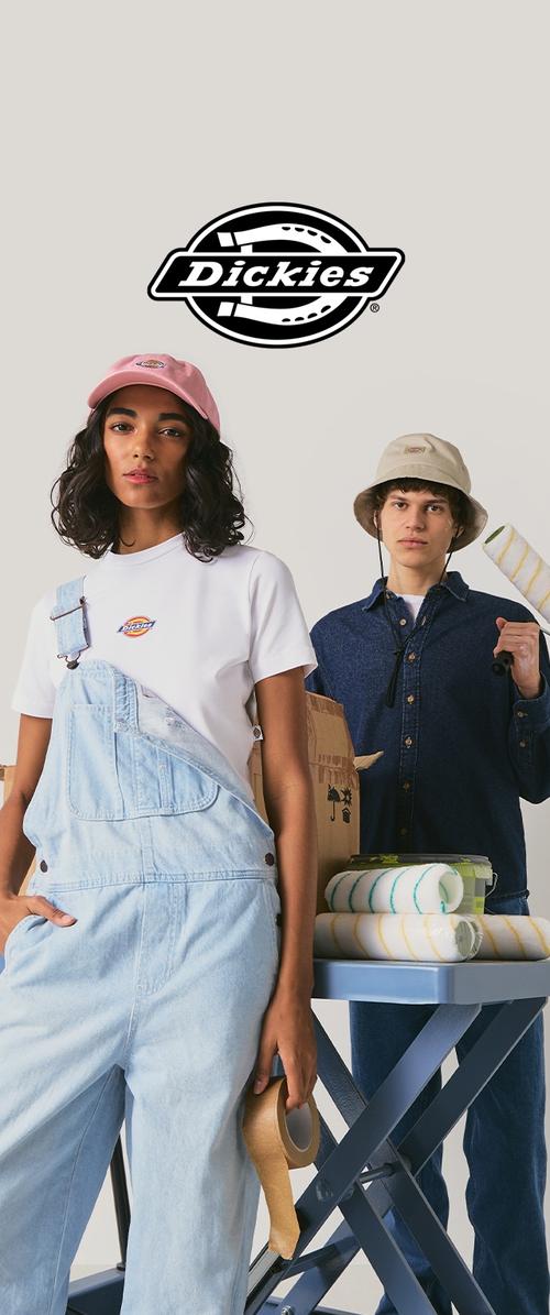 Dos personas vestidas con ropa y gorras Dickies, sosteniendo materiales de pintura como cinta y rodillo, con una mesa cercana llena de rodillos de pintura.
