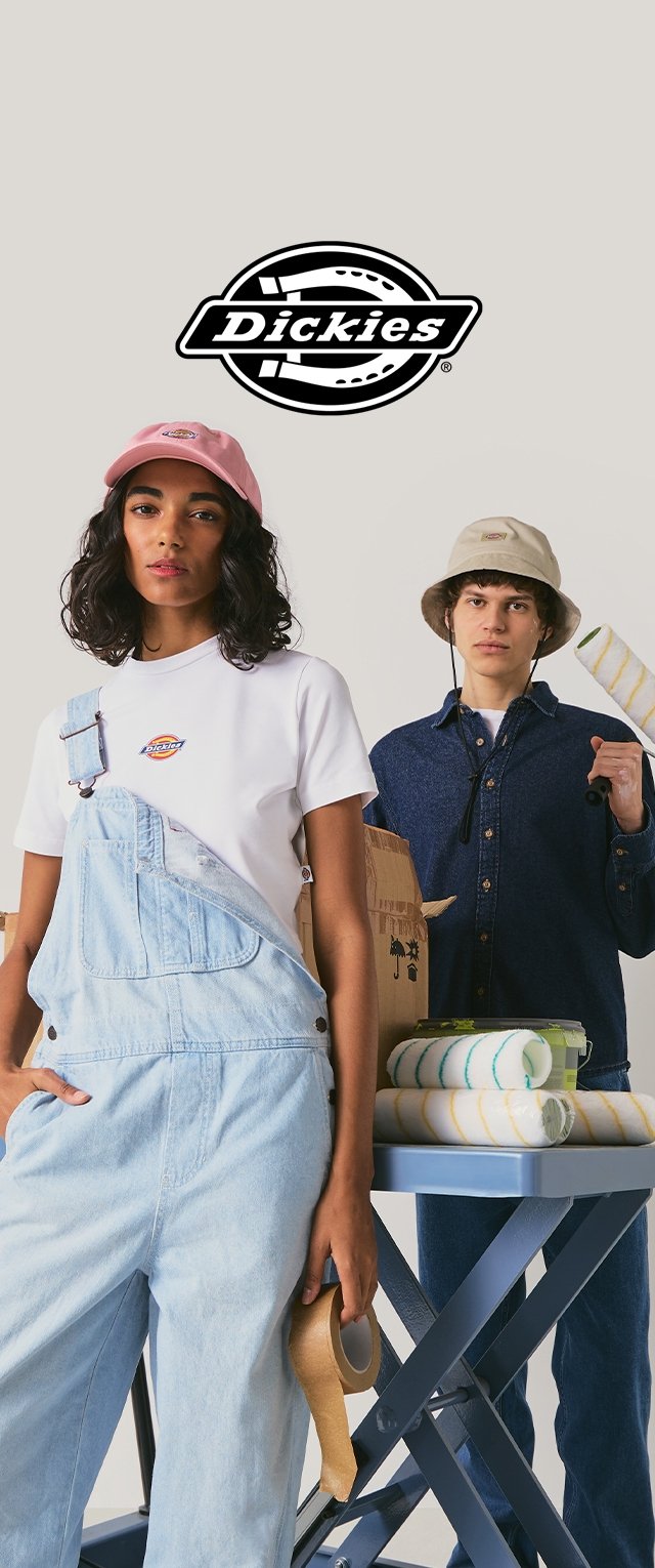 Dos personas vestidas con ropa y gorras Dickies, sosteniendo materiales de pintura como cinta y rodillo, con una mesa cercana llena de rodillos de pintura.