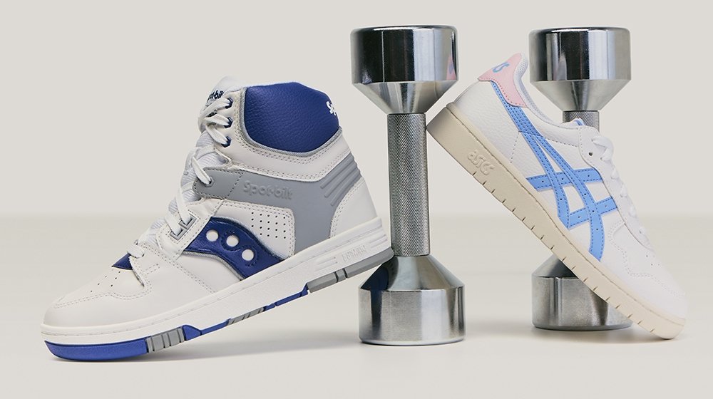 Zwei sportliche Sneakers, einer weiß mit blauen Akzenten und einer weiß mit rosa und blauen Streifen, balanciert auf silbernen Hanteln vor neutralem Hintergrund.