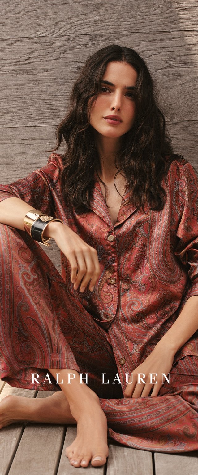 Punane ja paisley-mustriga siidist pidžaamakomplekt, millel on mugav lõige, koos nööbitava särgi ja lahtiste pükstega. Välimust täiendab kuldne käevõru.