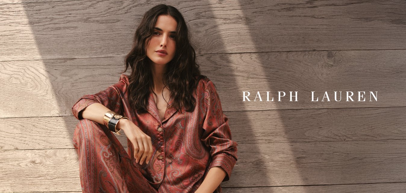 Červený saténový pyžamový set s paisley vzorem, zapínáním na knoflíky vpředu, dlouhými rukávy a volným střihem, doplněný jednoduchým náramkem s manžetou, na dřevěné terase.