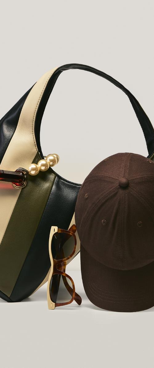 Schwarz-, Creme- und Oliv gestreifte Handtasche mit Perlendetails, Schildkrötensonnenbrille mit Creme-Akzenten und einer dunkelbraunen Baseballkappe.