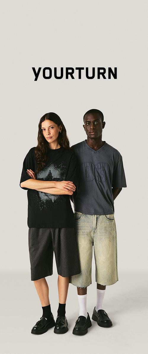 Zwei Models stehen nebeneinander und tragen lässige, übergroße Oberteile und lange Shorts, mit dem Text "YOURTURN" über ihnen vor einem neutralen Hintergrund.