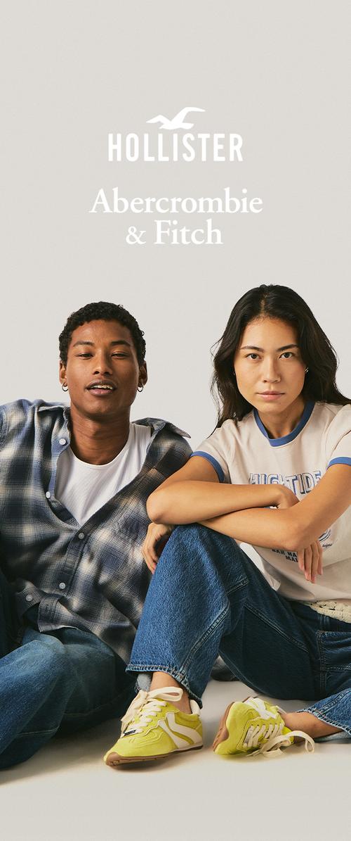 Zwei junge Erwachsene, ein Mann in einem karierten Hemd und eine Frau in einem T-Shirt und Jeans, sitzen entspannt unter den Logos von Hollister und Abercrombie & Fitch.