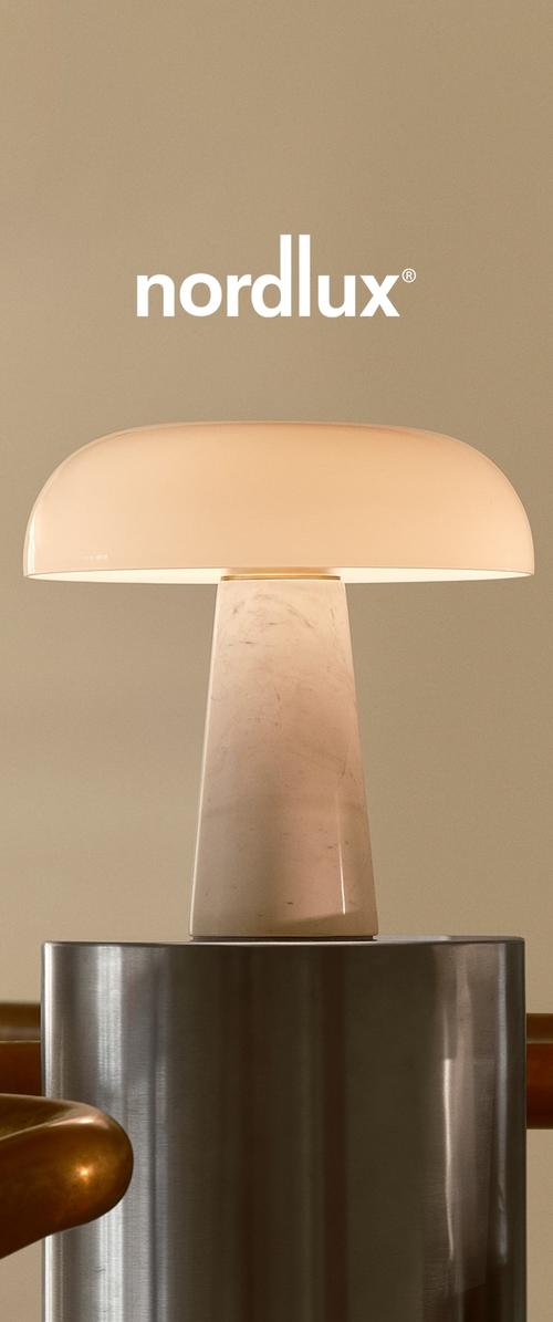 Lampa stołowa z zaokrąglonym, półprzezroczystym kloszem w delikatnej bieli, oparta na cylindrycznej marmurowej podstawie, umieszczona na metalowej powierzchni.