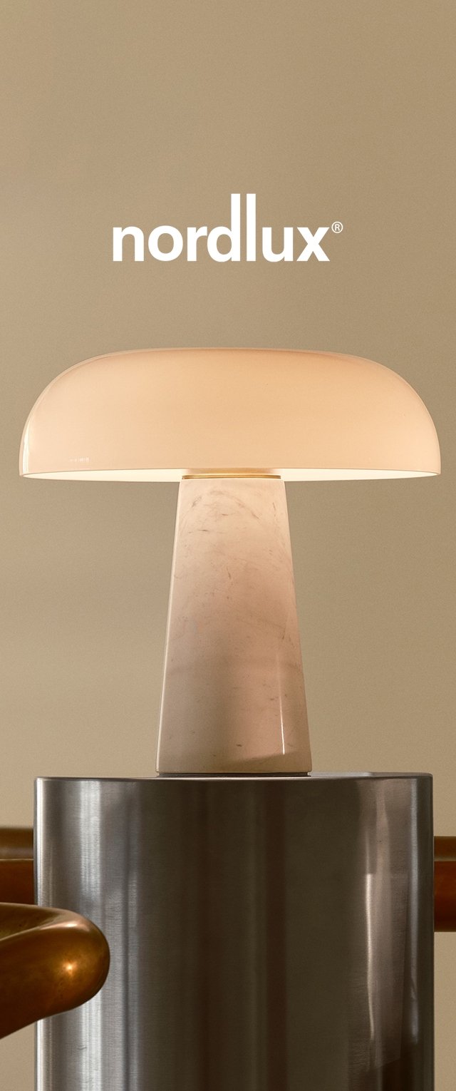 Lampa stołowa z zaokrąglonym, półprzezroczystym kloszem w delikatnej bieli, oparta na cylindrycznej marmurowej podstawie, umieszczona na metalowej powierzchni.