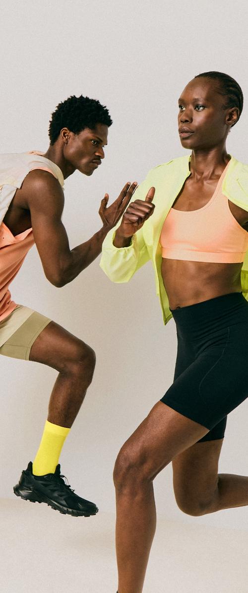 Deux personnes athlétiques en tenue de sport font du jogging sur place devant un fond uni, concentrées sur leur mouvement et leur posture.