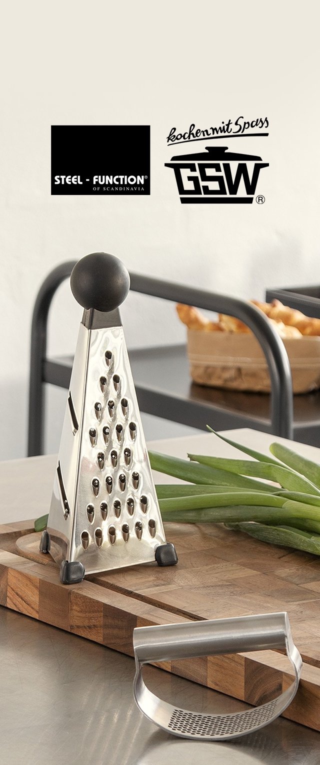 Rasp van roestvrij staal en gebogen groenteschiller op houten snijplank met lente-uitjes en broodmand op de achtergrond.