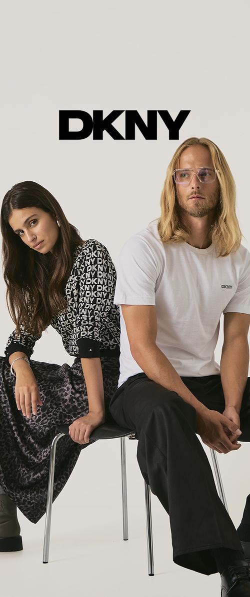 Abbigliamento DKNY; donna in felpa nera con grafica e gonna con stampa leopardo, uomo in t-shirt bianca DKNY e pantaloni neri, entrambi seduti su delle sedie.