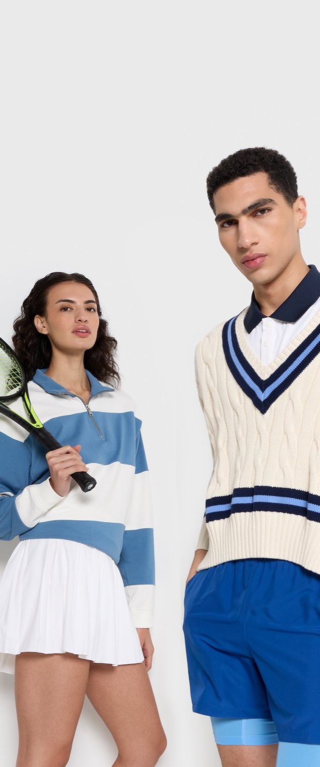 Blau-weißer gestreifter Langarm-Top, weißer plissierter Rock; cremefarbener Kabelstrick-Westen mit marinefarbenen Akzenten, blaue Shorts, Tennisschläger.