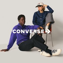 Dva lidé v běžném oblečení; jeden sedí na podlaze v fialovém svetru, černých kalhotách a bílých botách; druhý na židli v denimové bundě, šedých kalhotách a bílé čepici.