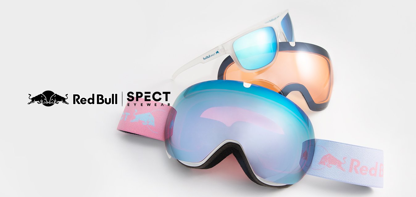 Dvoje lyžařských brýlí: jedny s velkým modrým sklem a růžovým páskem s logem Red Bull; druhé s oranžovým sklem a bílým rámem.