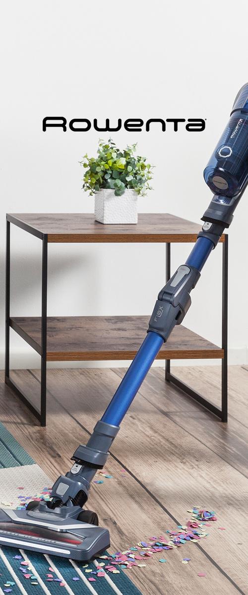 Aspiradora inalámbrica con un cuerpo azul y acentos grises, mango flexible y una cabeza de limpieza de perfil bajo sobre un suelo de madera con confeti disperso.