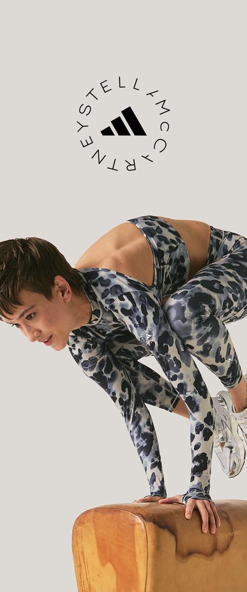 Femme en tenue de sport à motifs faisant l'équilibre sur les mains sur une selle de gymnastique en bois, avec le logo Stella McCartney au-dessus.