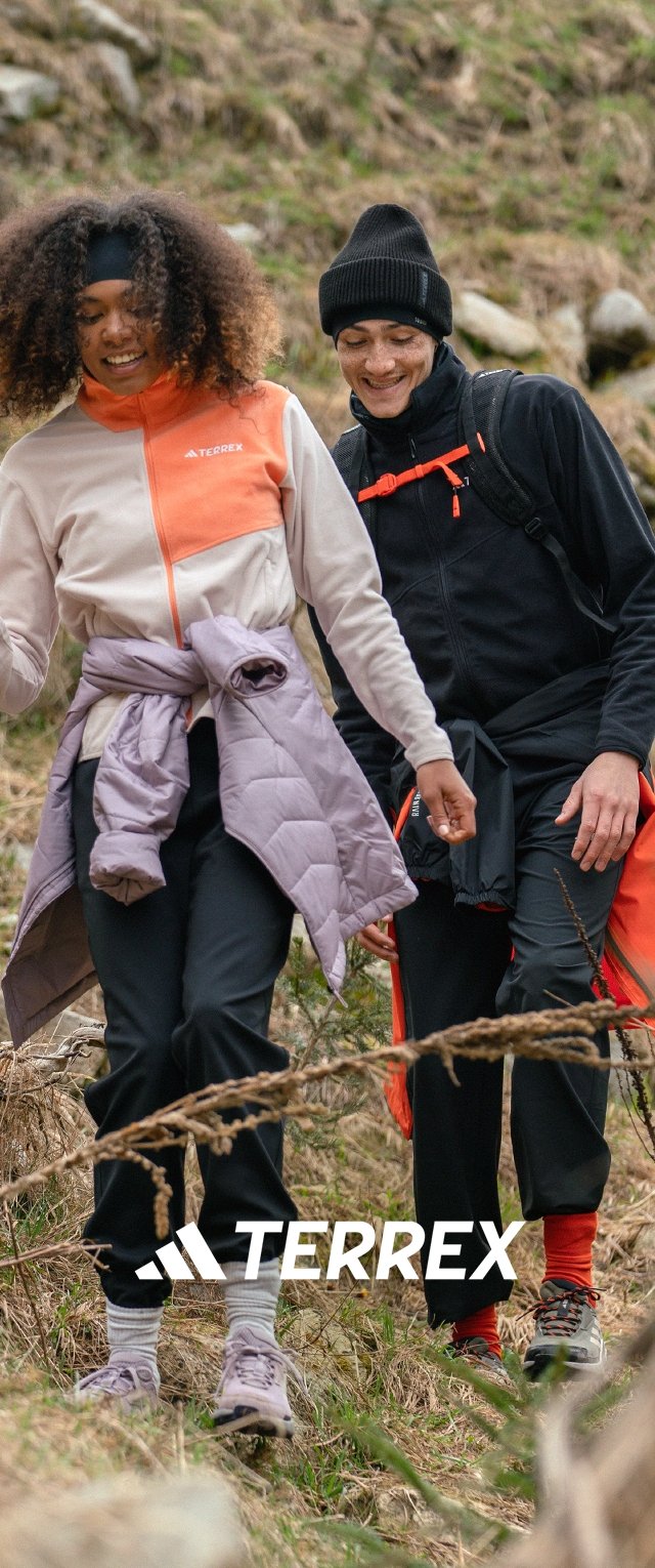 To personer går på en sti. Den ene har en lyserød og orange jakke på med sorte bukser, den anden har en sort jakke og røde bukser.