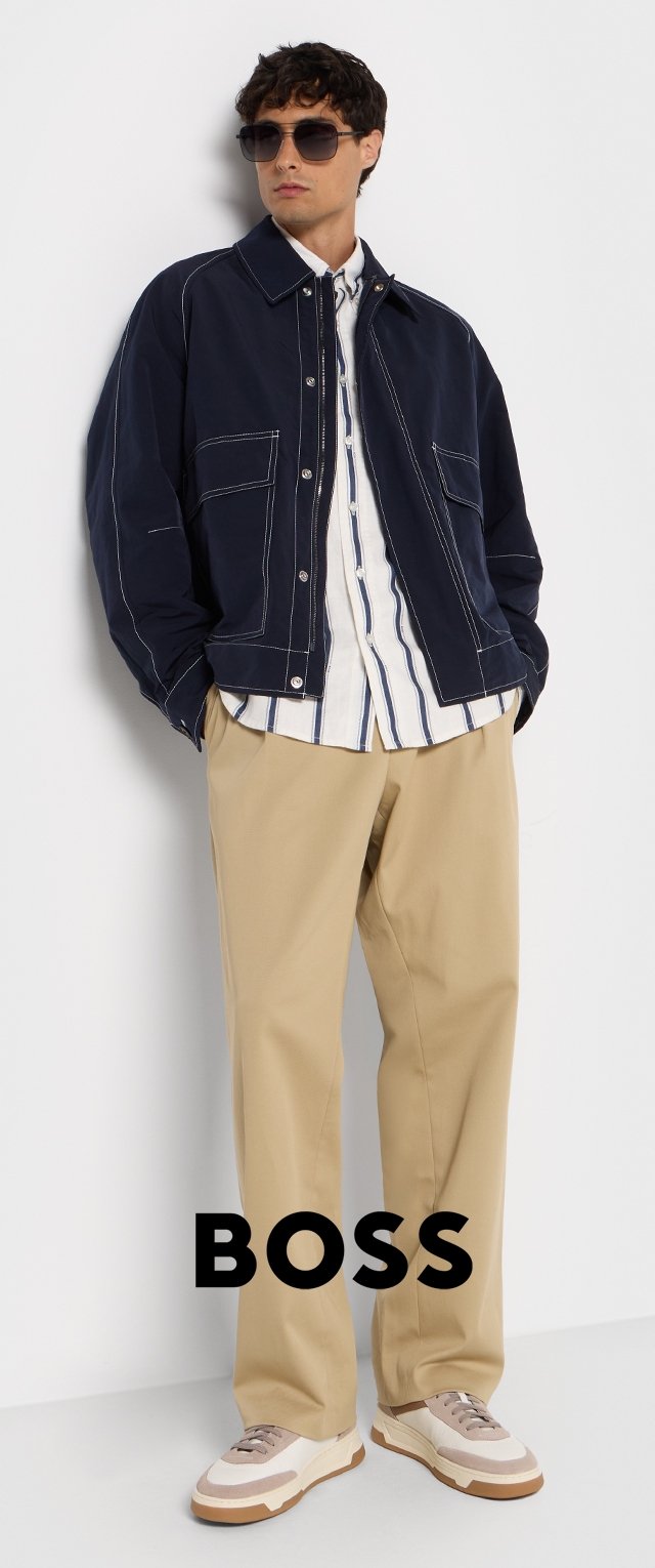 Veste bleu marine avec des coutures blanches, chemise rayée blanche, pantalon beige et baskets bicolores. Des lunettes de soleil complètent le look.