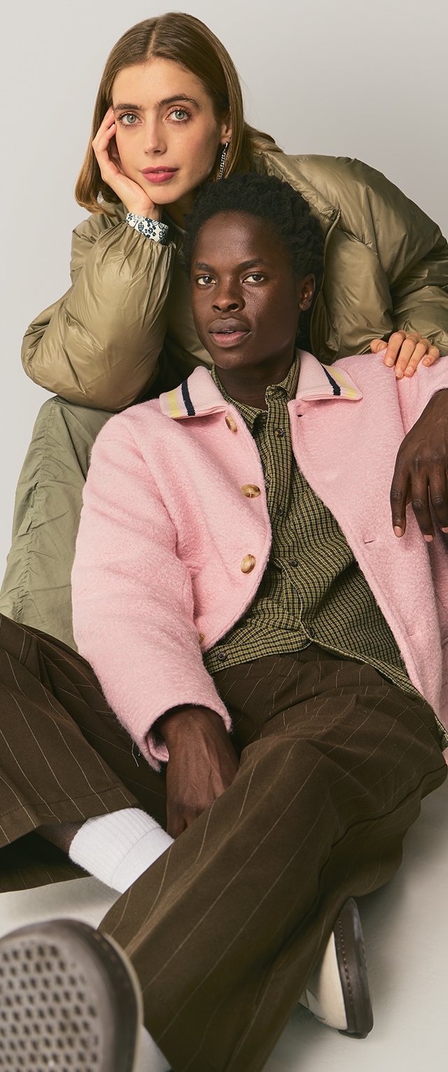 Roze donzige jas met gouden knopen, groene pufferjack, gestreepte kraag, geruit shirt, bruine gestreepte broek en witte sokken.