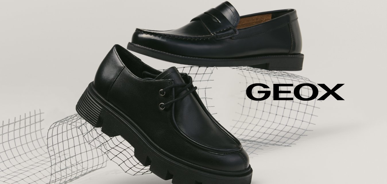 Dva černé kožené boty zobrazené na bílém povrchu, jeden mokasín s prošíváním a jeden šněrovací s masivní podrážkou, umístěné na zakřivené drátěné síti.