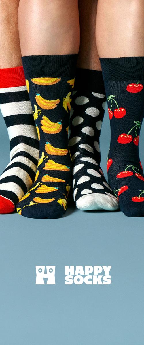 Cuatro personas llevan calcetines Happy Socks de colores con estampados de plátanos, cerezas, lunares y rayas sobre un fondo azul.