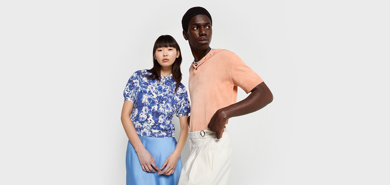 Dva modelky stojí blízko sebe. Jedna má na sobě modrý květinový top s krátkými rukávy a světle modrou sukni. Druhá má na sobě oranžový svetr s krátkým rukávem a bílé kalhoty.