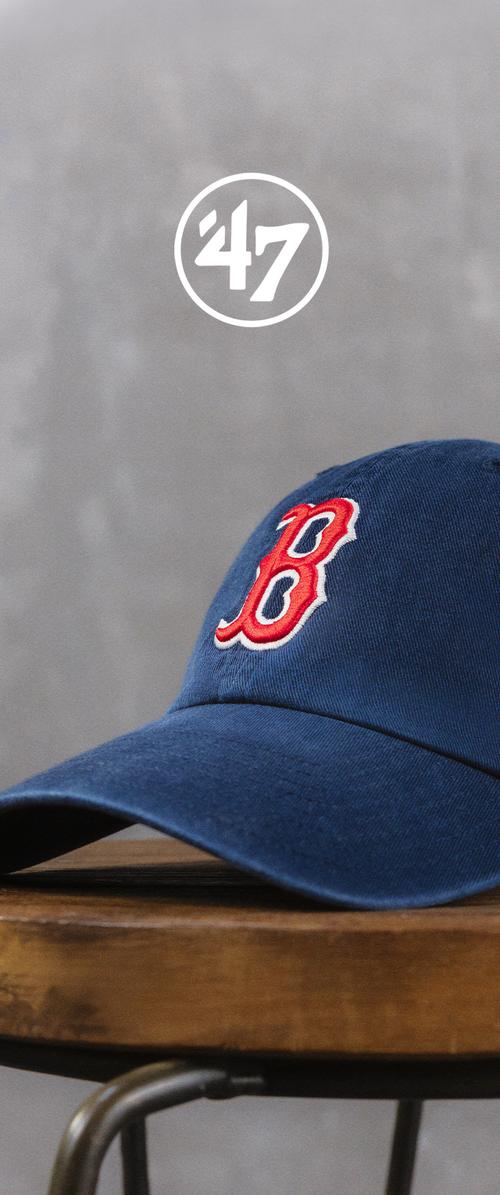Blue baseball cap with a red and white embroidered letter "B" resting on a wooden stool against a gray background.